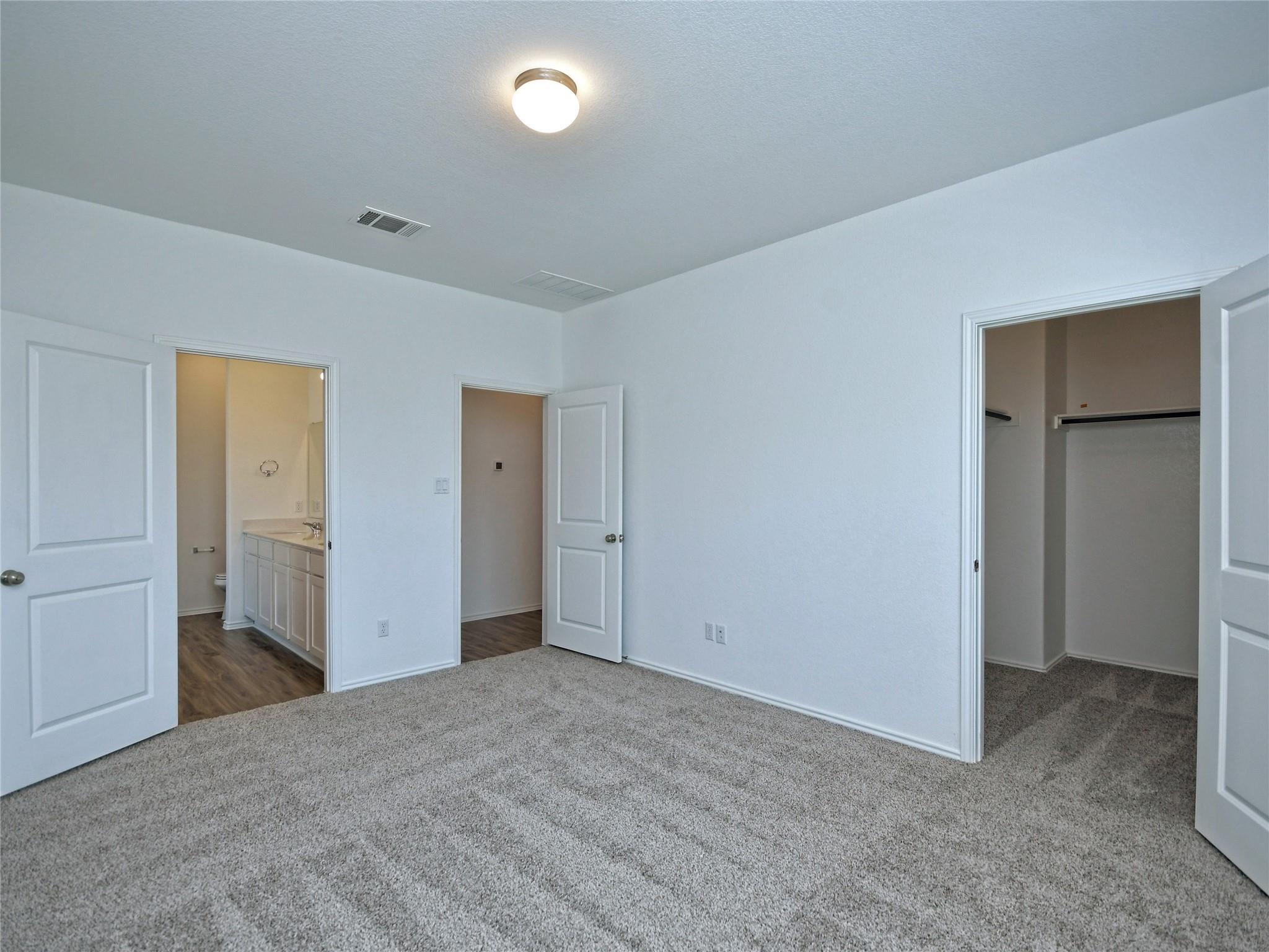 Empty carpeted bedroom with an ensuite bathroom and open walk-in closet.