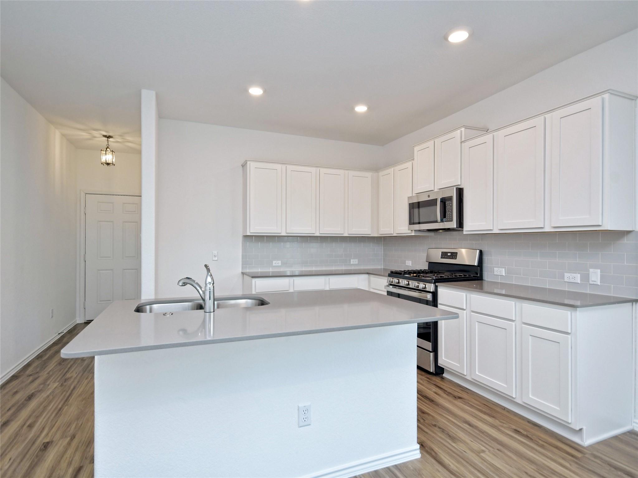 Kitchen with white shaker cabinets, stainless appliances, and a large island sink.