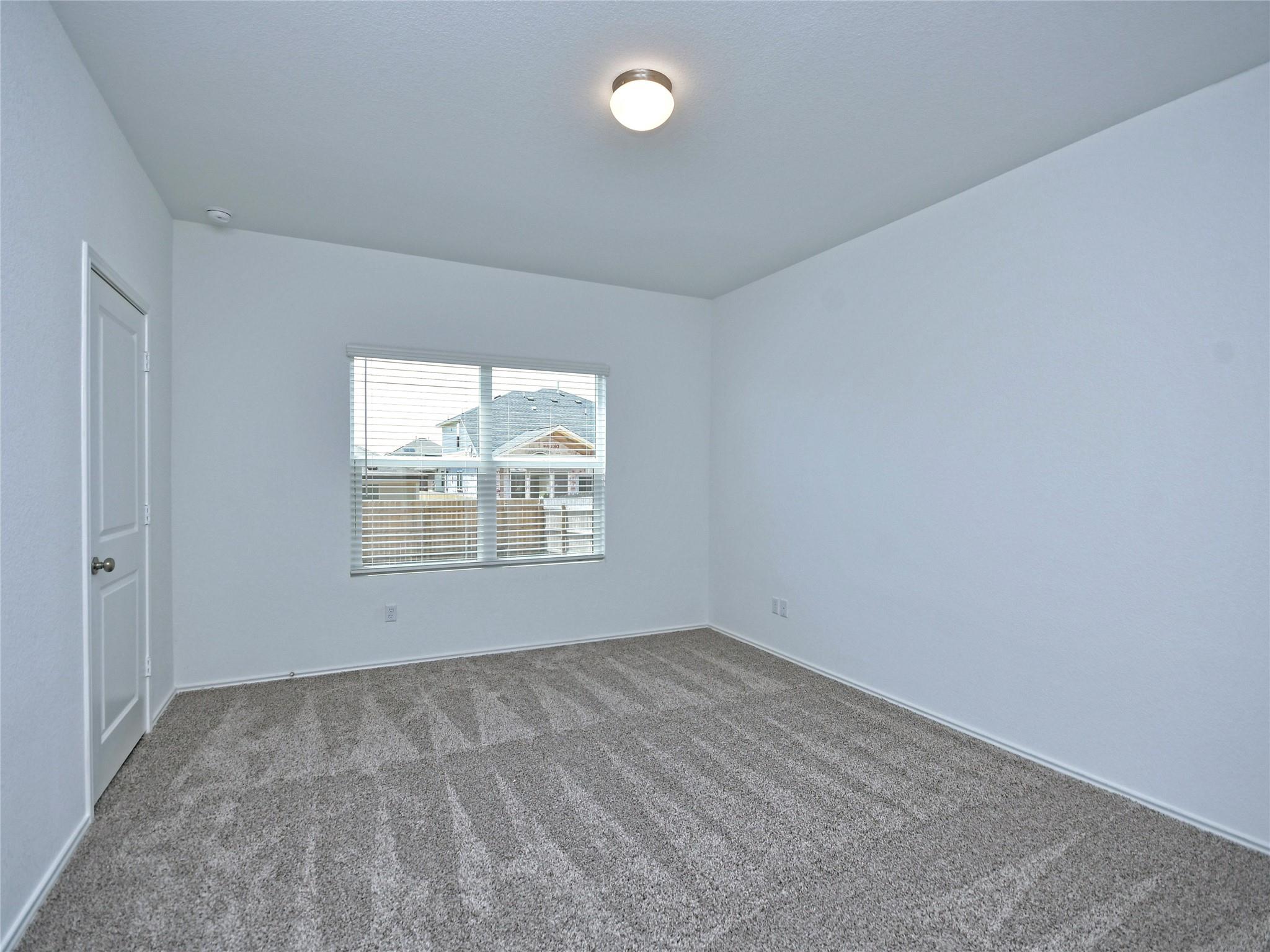 Empty bedroom with gray carpet, white walls, and a window with blinds.