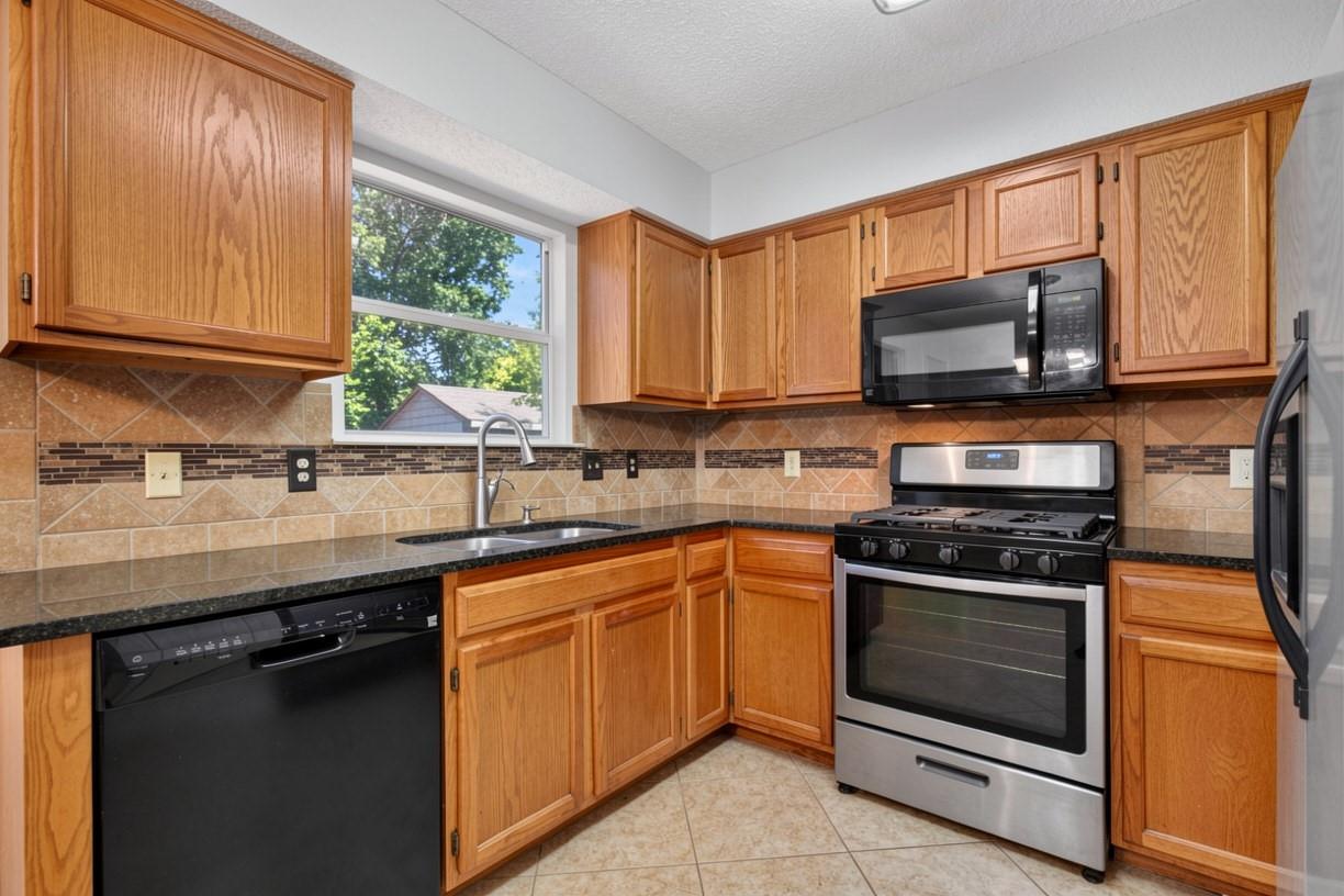 Kitchen with honey-colored wood cabinets, tiled backsplash, and stainless steel range and microwave.