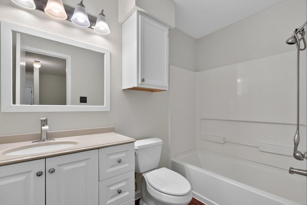Bathroom with white vanity, framed mirror, toilet, and bathtub with wall-mounted shower.