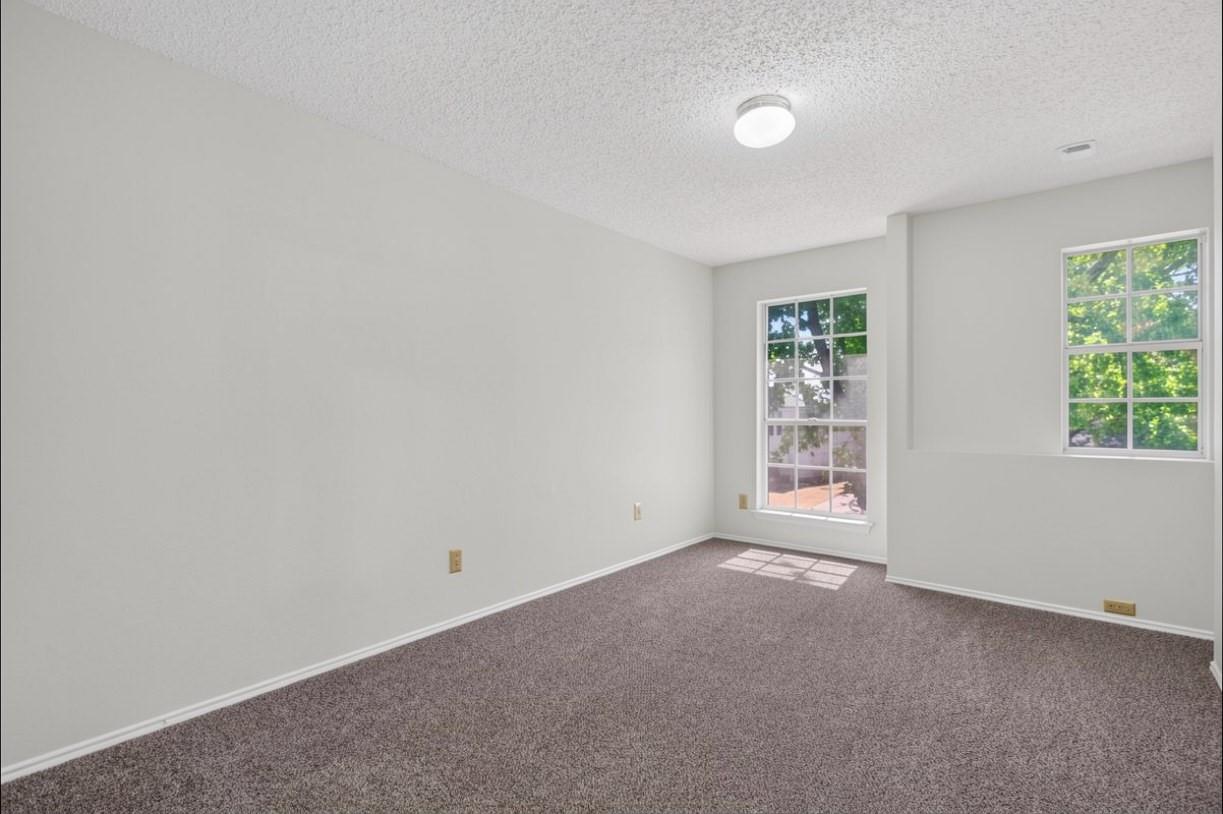 Empty carpeted bedroom with two windows and light gray walls.