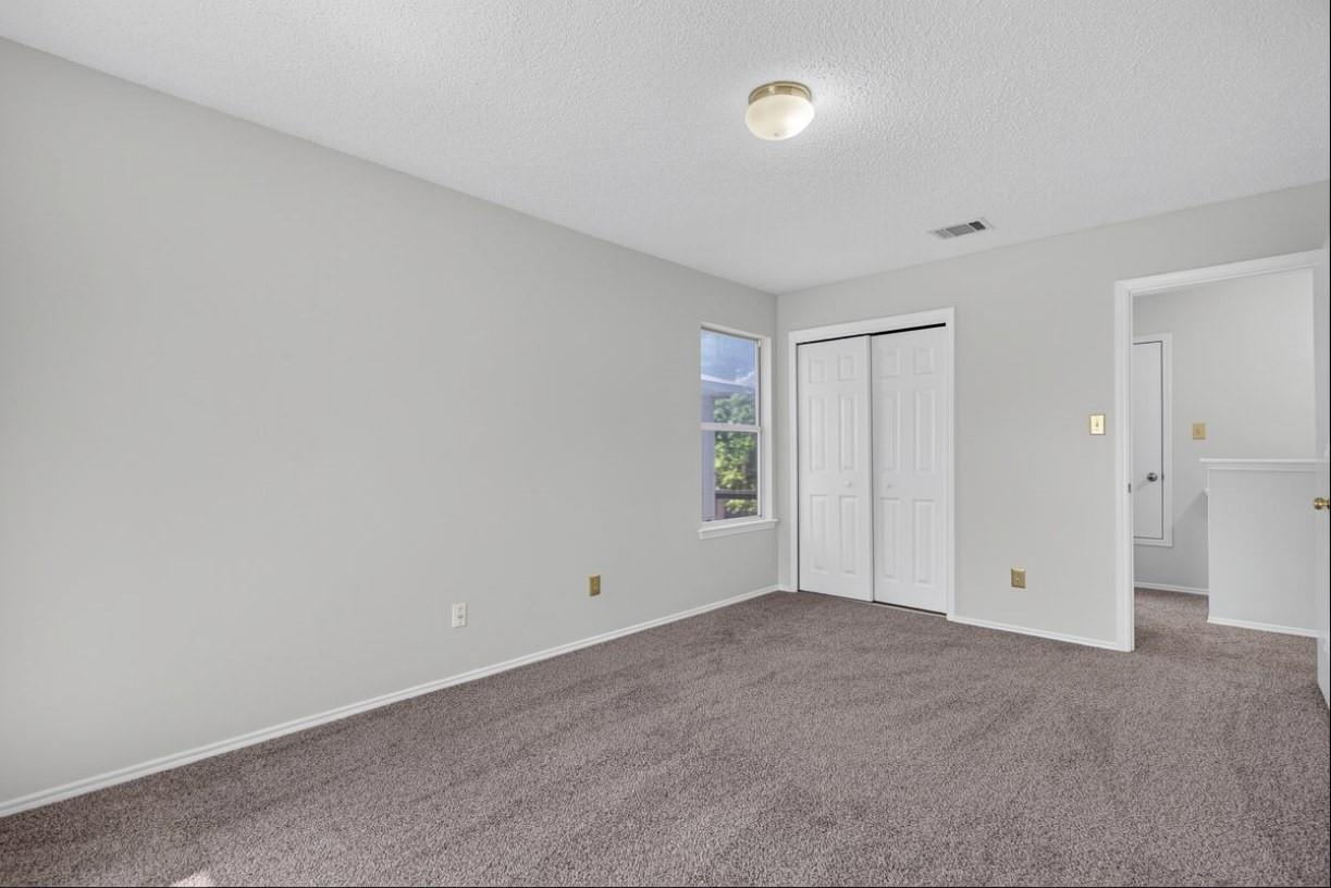 Vacant bedroom with carpet, a double-door closet, and a window beside the hallway doorway.
