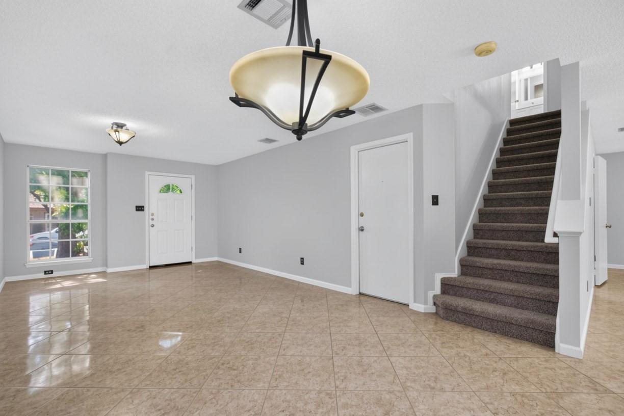 Unfurnished entry with a tiled floor, front door, and carpeted staircase with white railing.