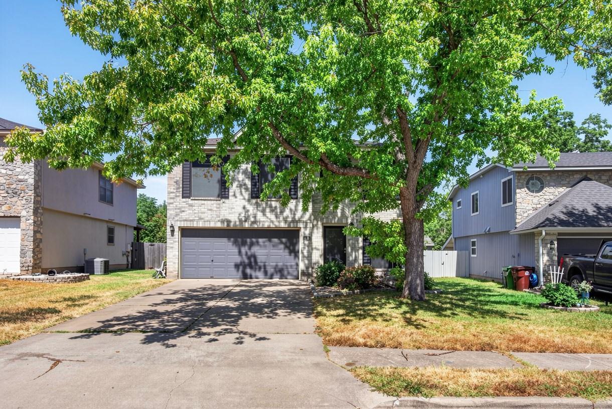 Two-story stone house with a double garage and driveway beneath a large leafy tree.