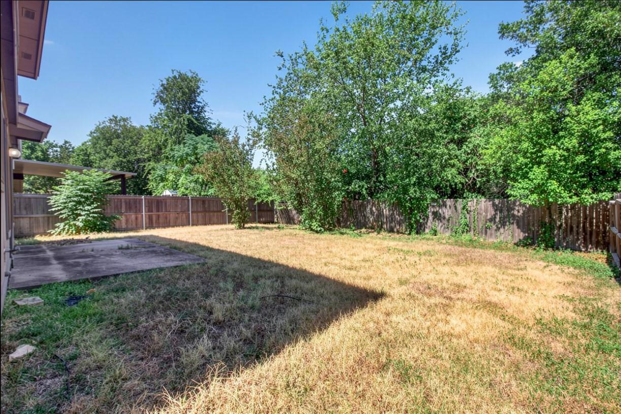 Backyard with a concrete patio, wooden privacy fence, and mature trees.