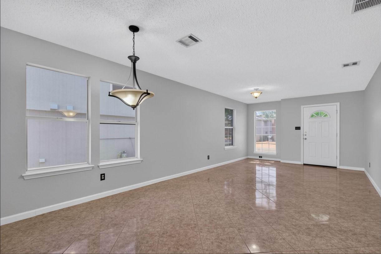 Empty living room with glossy tile floors, two windows, and a chandelier.