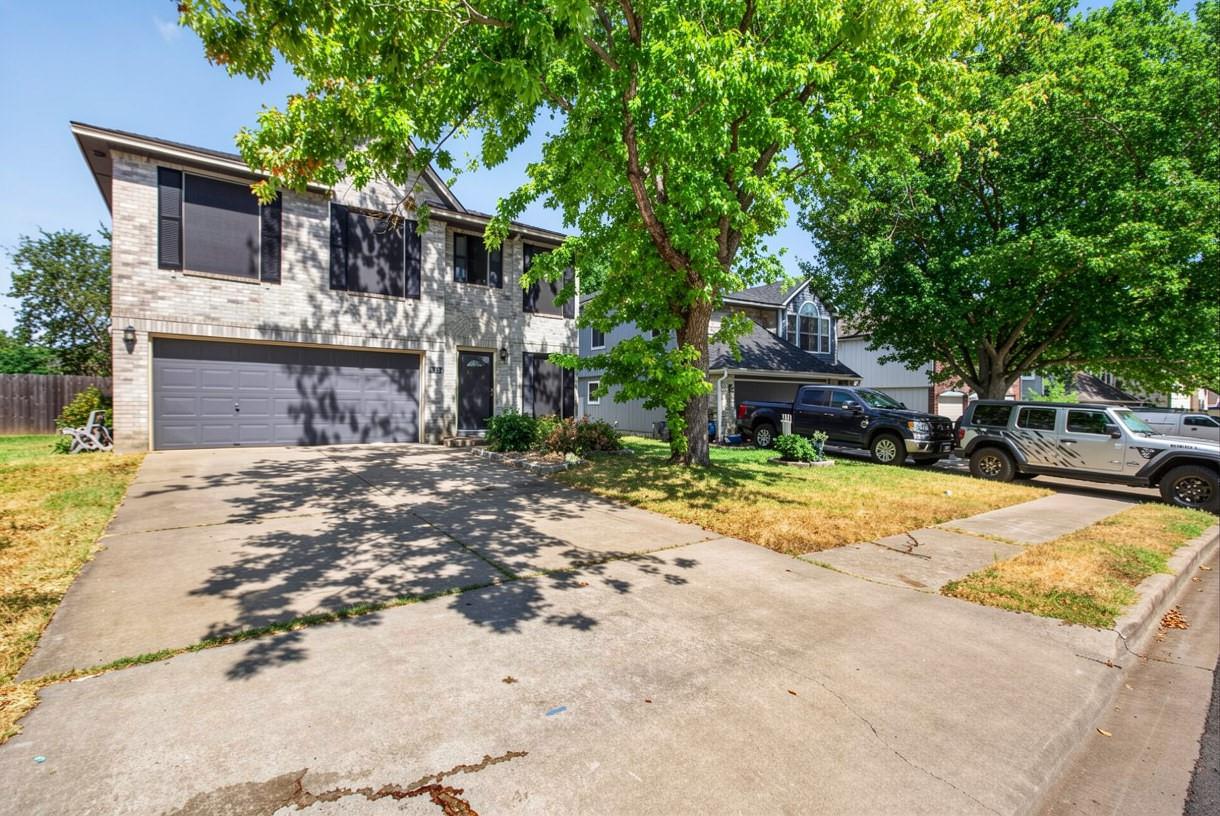 Two-story brick house with a double garage and broad driveway beneath mature shade trees.