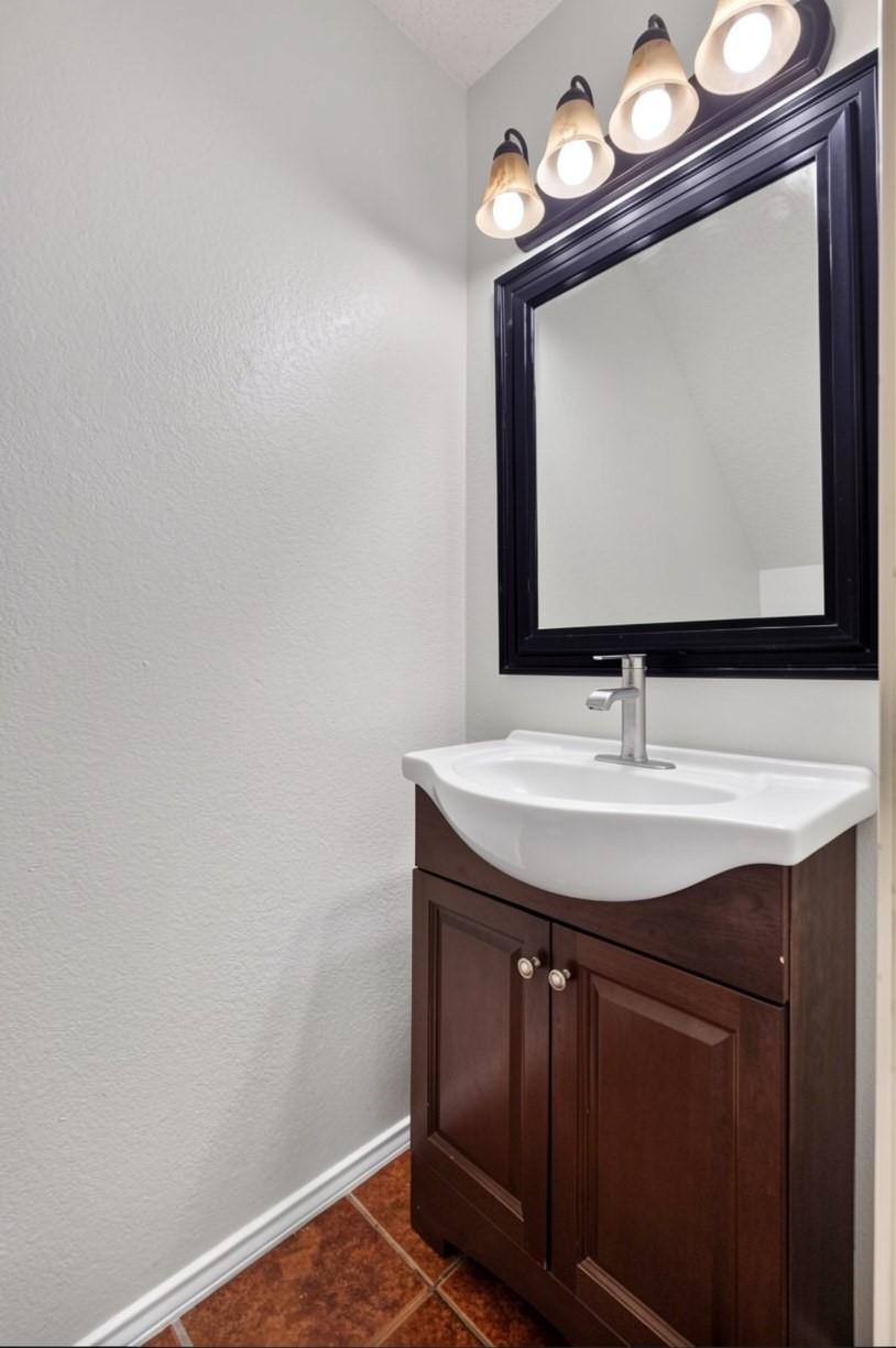 Bathroom vanity with a dark wood cabinet, white sink, black-framed mirror, and four lights.
