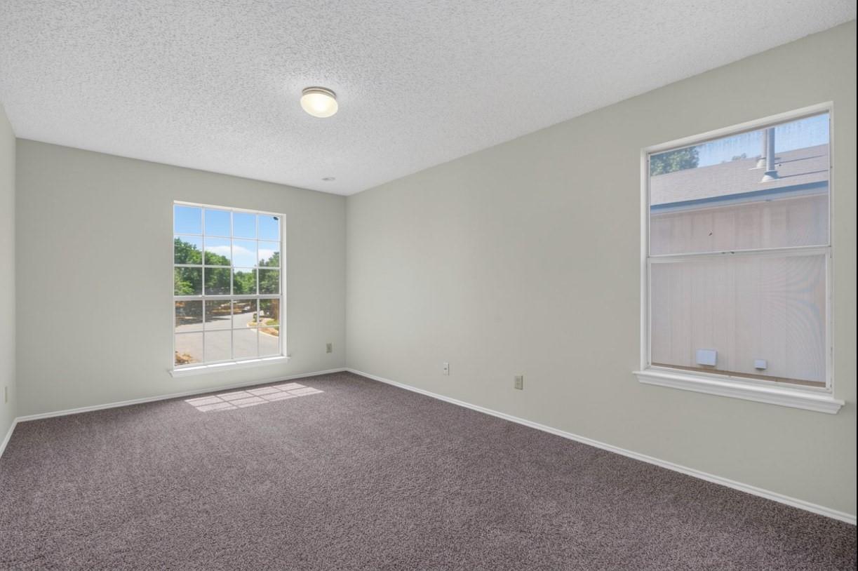 Empty carpeted bedroom with light gray walls and two windows.