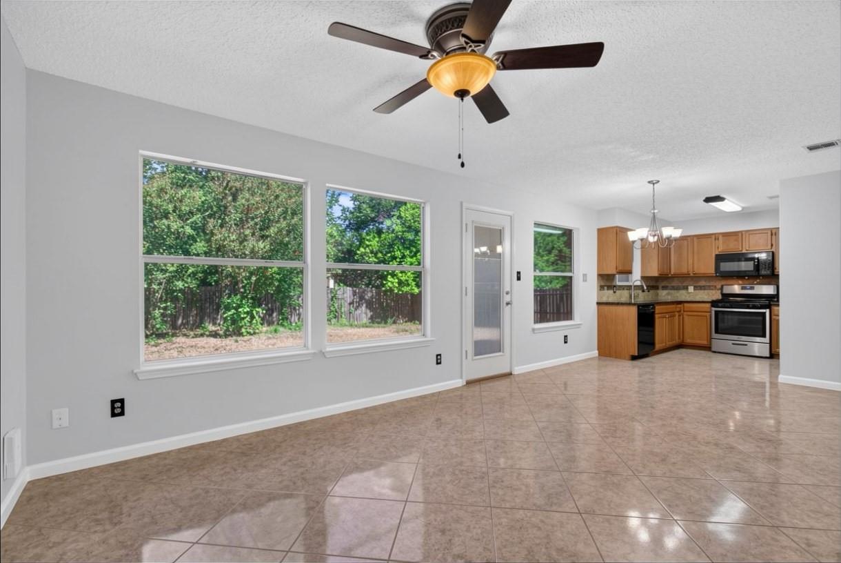 Open living area with tiled floors, large backyard-facing windows, and a wood-cabinet kitchen.