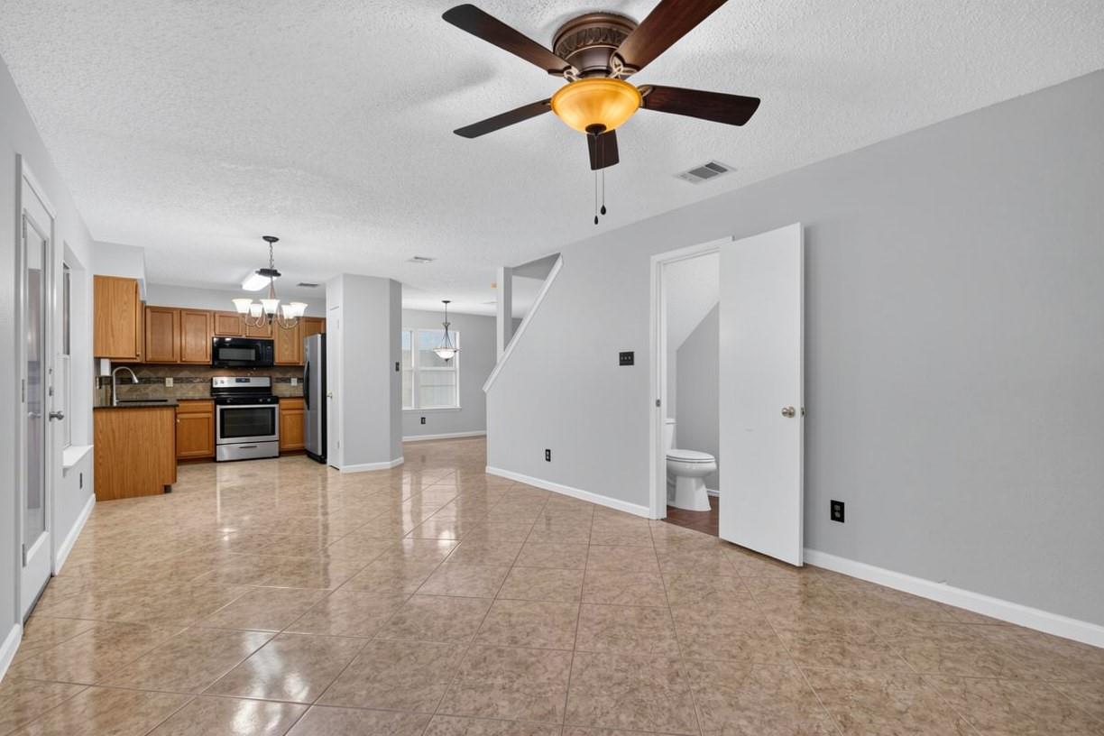 Open living and dining area with beige tile floors, ceiling fan, and adjoining wood-cabinet kitchen.