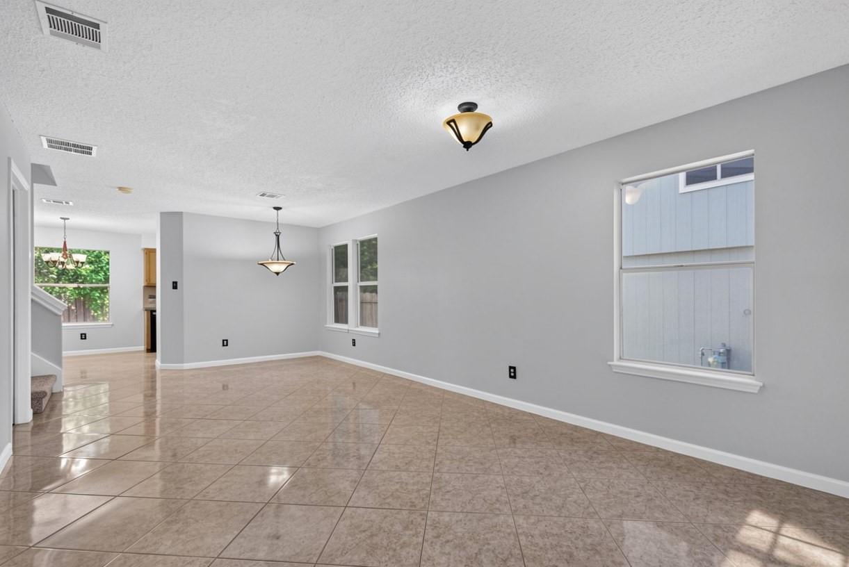 Empty living and dining area with glossy tile floors, gray walls, and large windows.