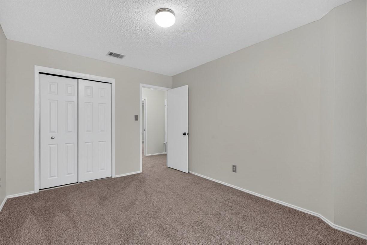 Unfurnished bedroom with beige carpet, sliding closet doors, and an open doorway.