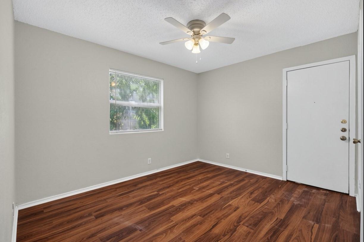Empty room with dark wood flooring, a ceiling fan, window blinds, and a white entry door.