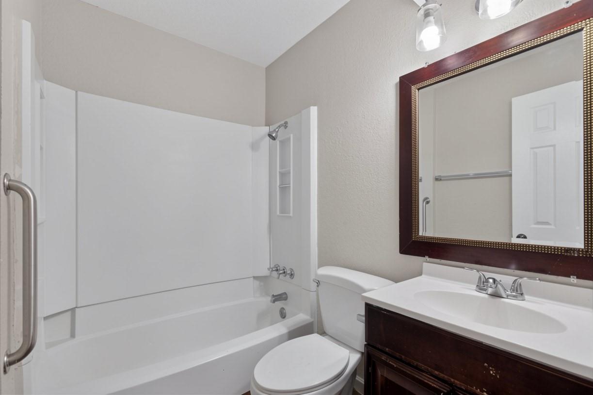 Bathroom with a white tub and shower, toilet, and dark wood vanity.