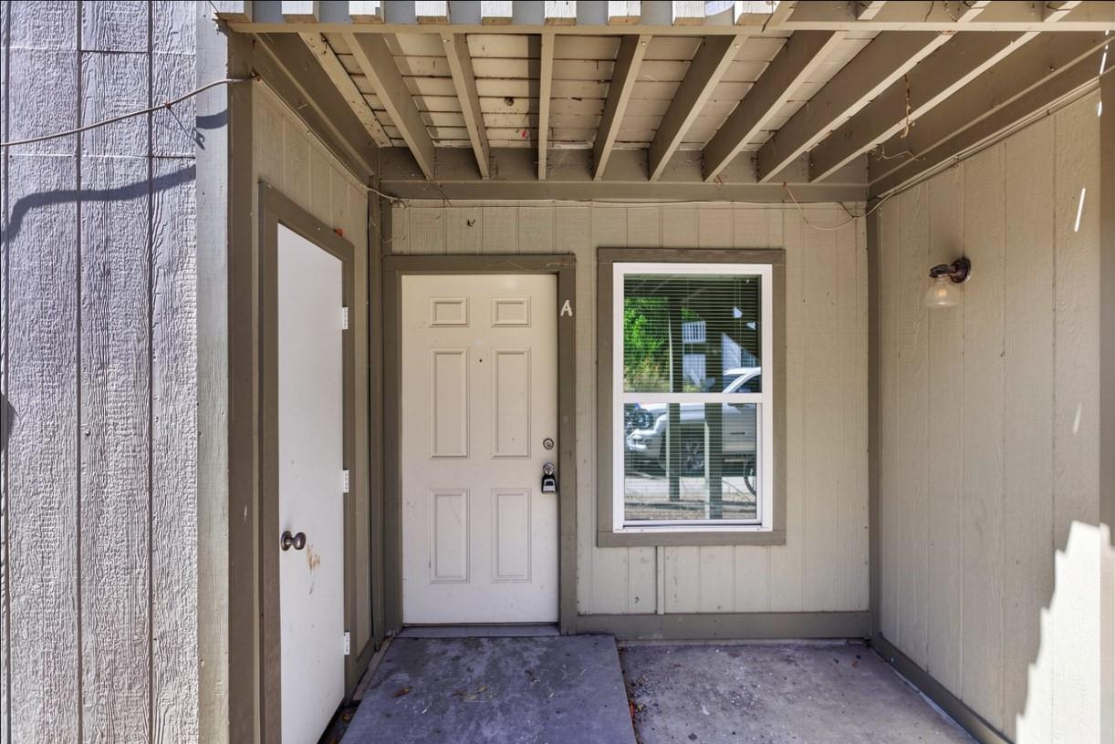 Covered exterior entry with a paneled front door, adjacent window, and concrete porch.