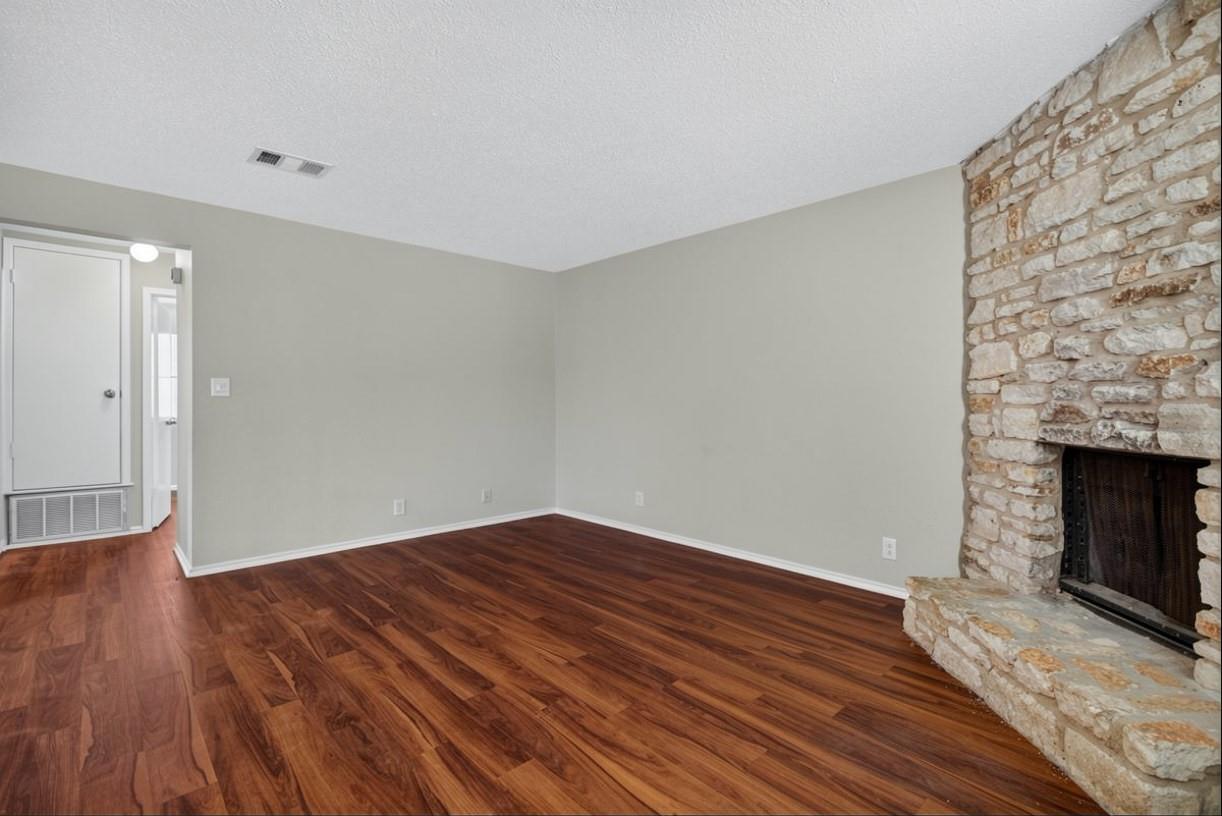 Empty living room with reddish-brown hardwood floors and a natural stone fireplace.