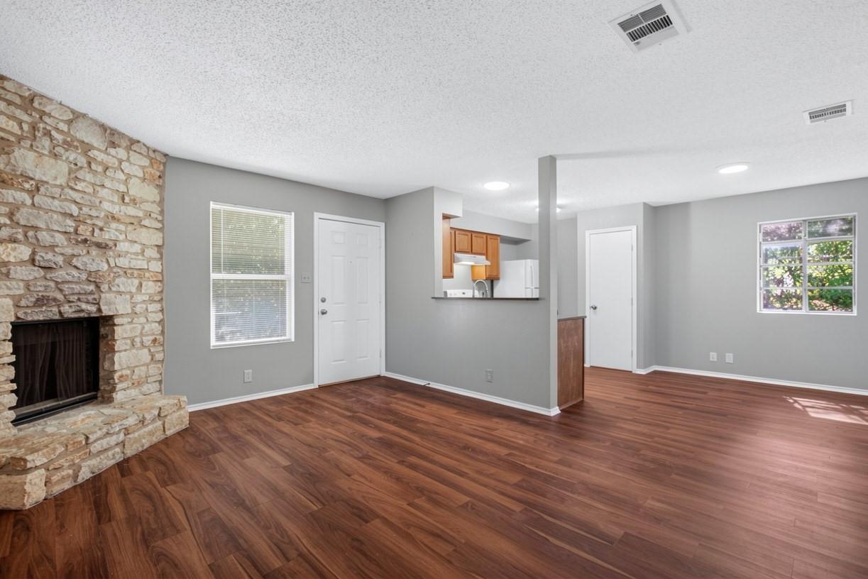 Unfurnished living room with a stone fireplace, dark wood floors, and an open kitchen.