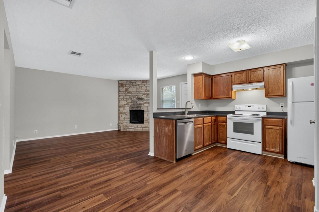 Open living room and kitchen with wood floors, wood cabinets, and a stone fireplace.