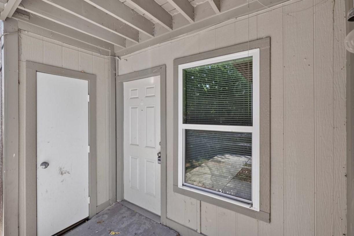 Covered entry with two white doors and a window with blinds.
