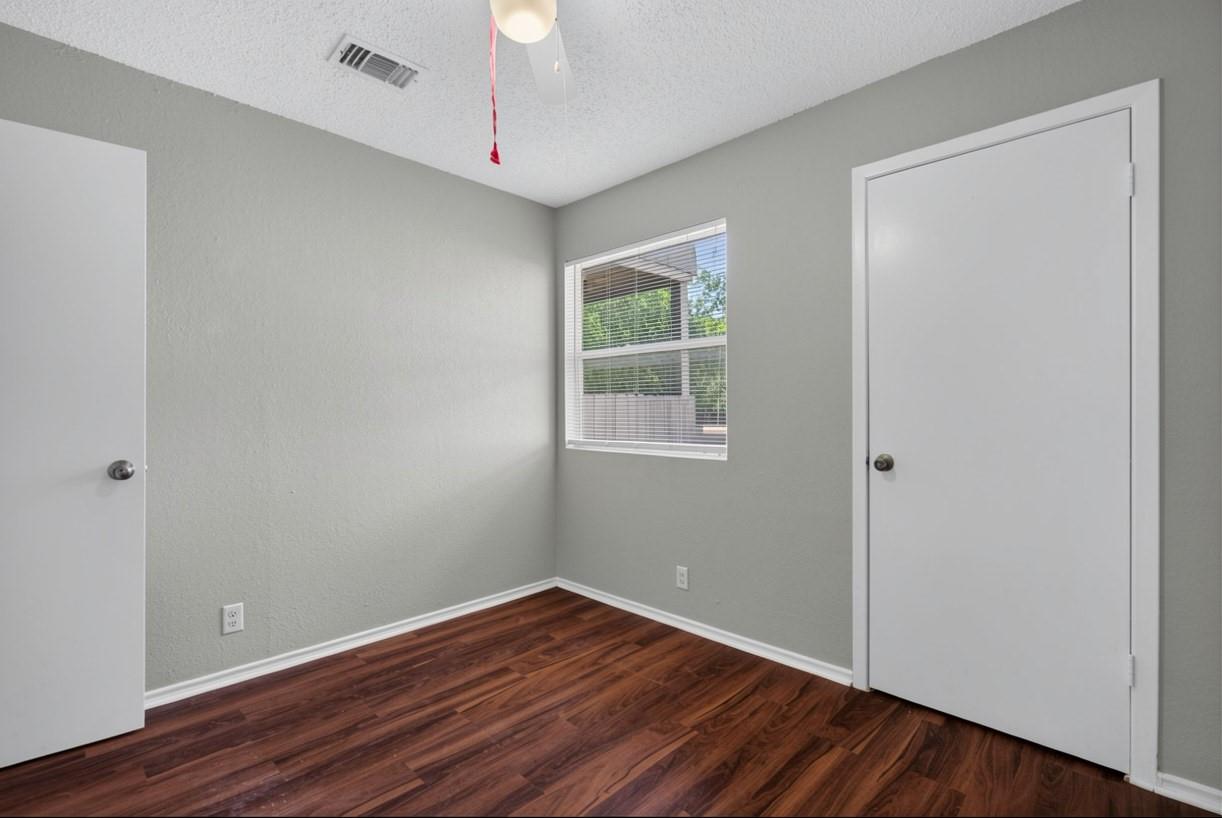 Empty bedroom with dark wood-look flooring, gray walls, and a window with blinds.