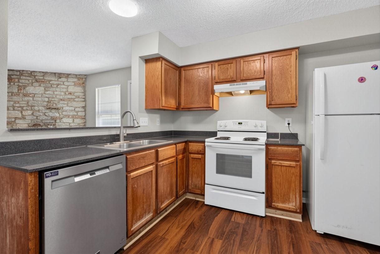 Kitchen with warm wood cabinets, dark countertops, and a stone accent wall.