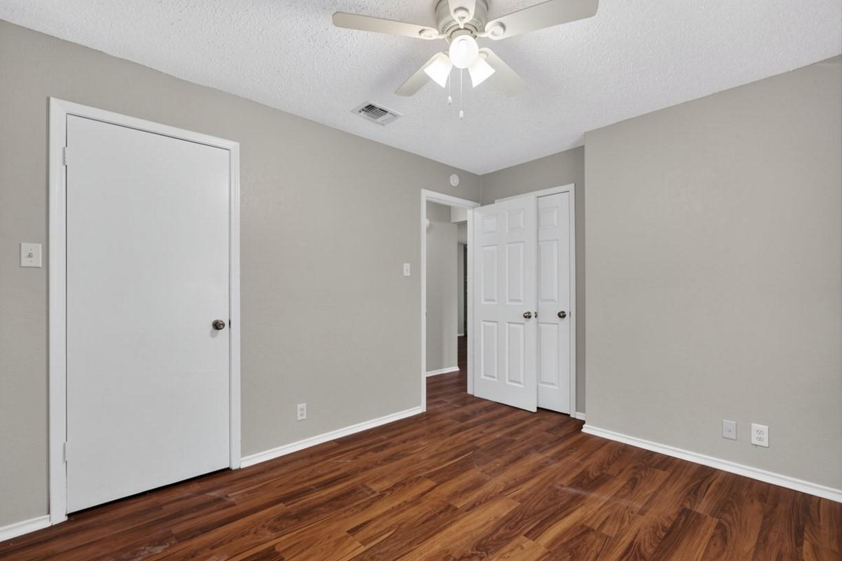 Empty bedroom with hardwood floors, white doors, and a ceiling fan with light.