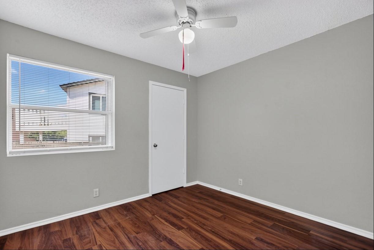 Empty room with reddish-brown flooring, a ceiling fan, and a window with blinds.