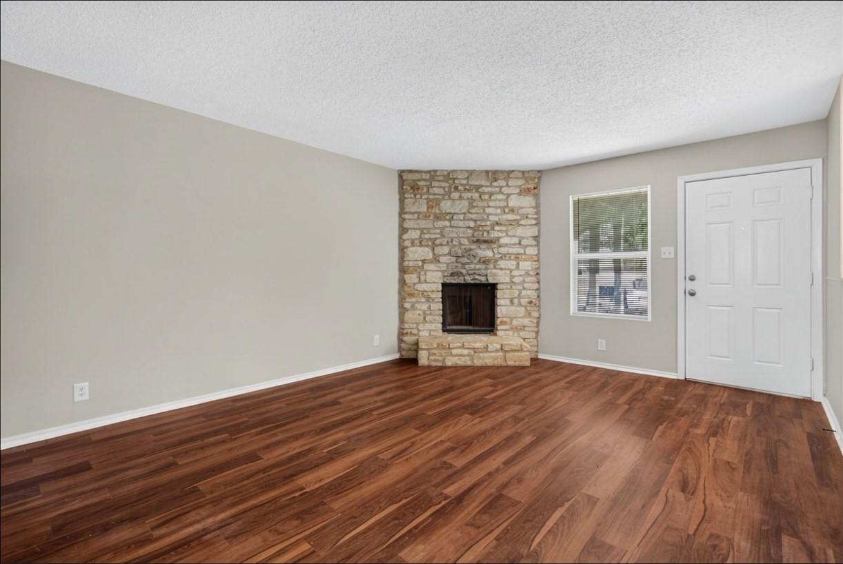 Unfurnished living room with a stone fireplace and reddish-brown wood flooring.
