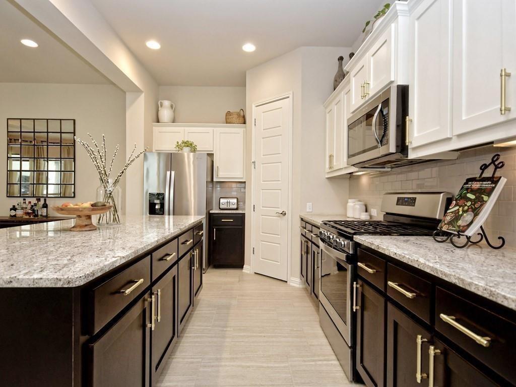 Galley kitchen with granite counters, dark cabinetry, stainless steel appliances, and a large island.