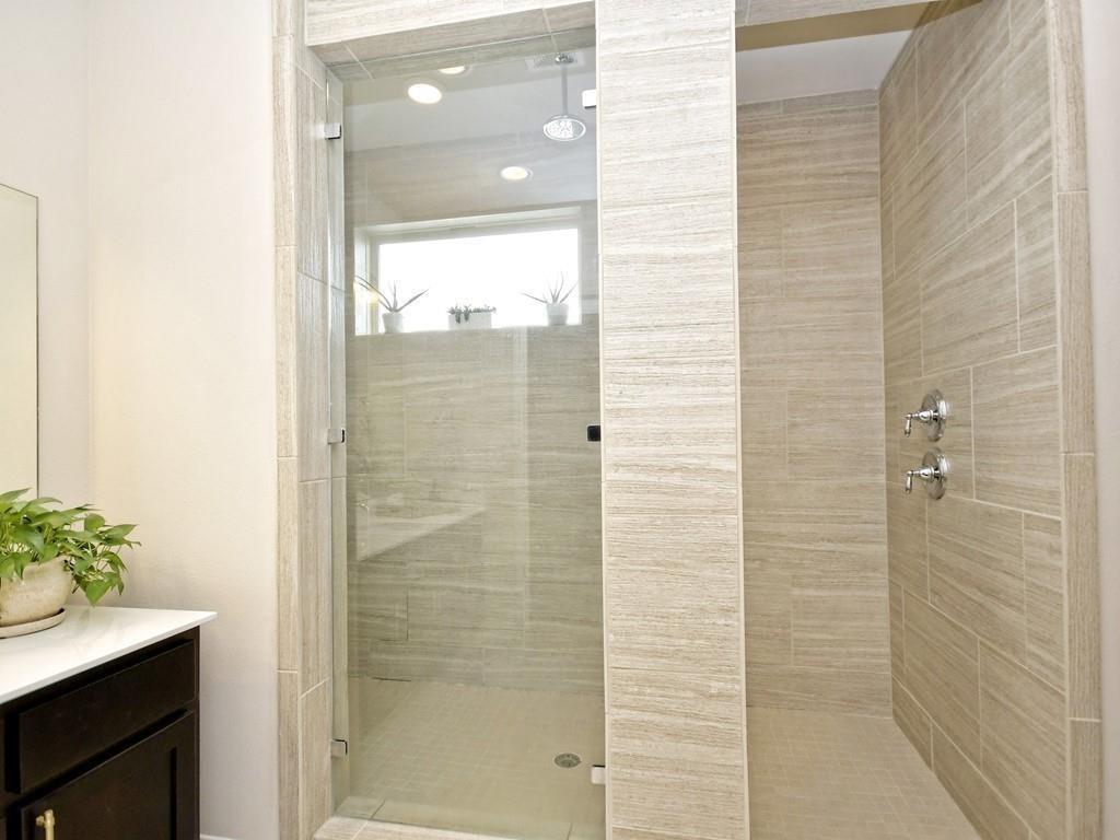 Modern tiled walk-in shower with clear glass enclosure and chrome fixtures.