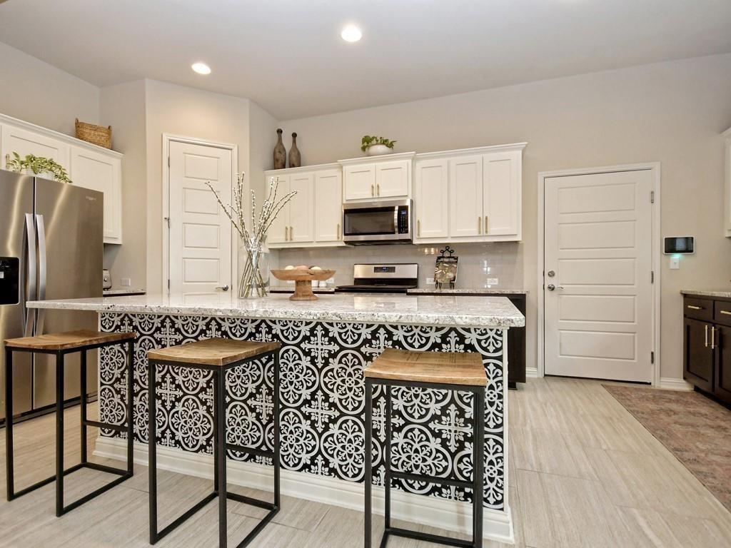 Kitchen with a patterned island front, three wooden stools, white cabinets, and stainless steel appliances.
