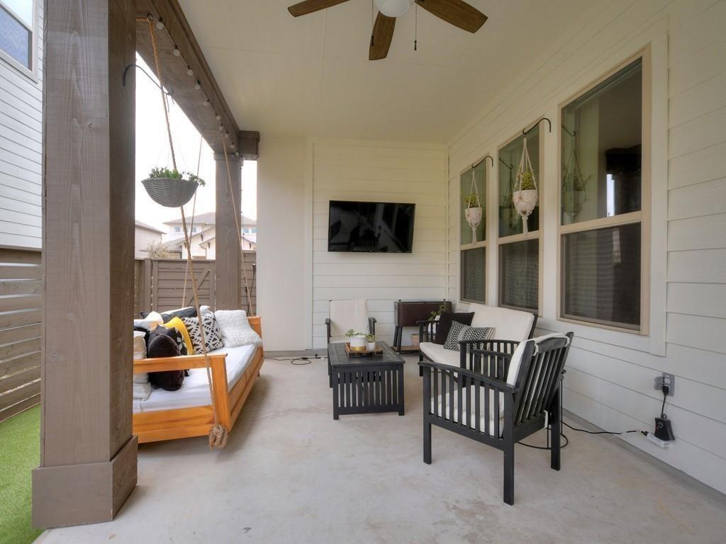 Covered patio with a wooden cushioned sofa, black chairs, hanging planters, and ceiling fan.