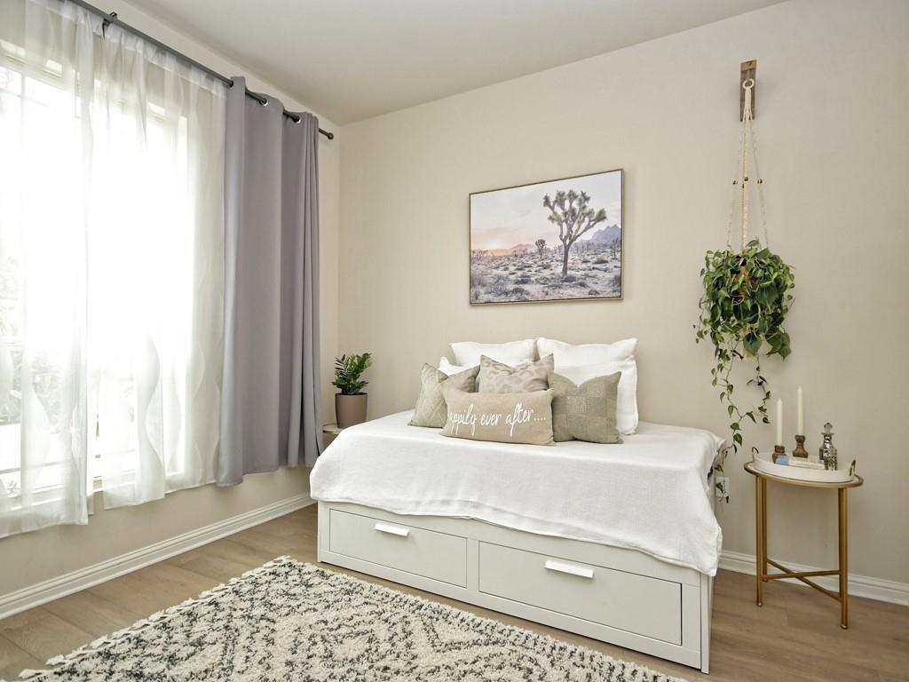 Staged bedroom with a white drawer bed, hanging plant, and large curtained window.
