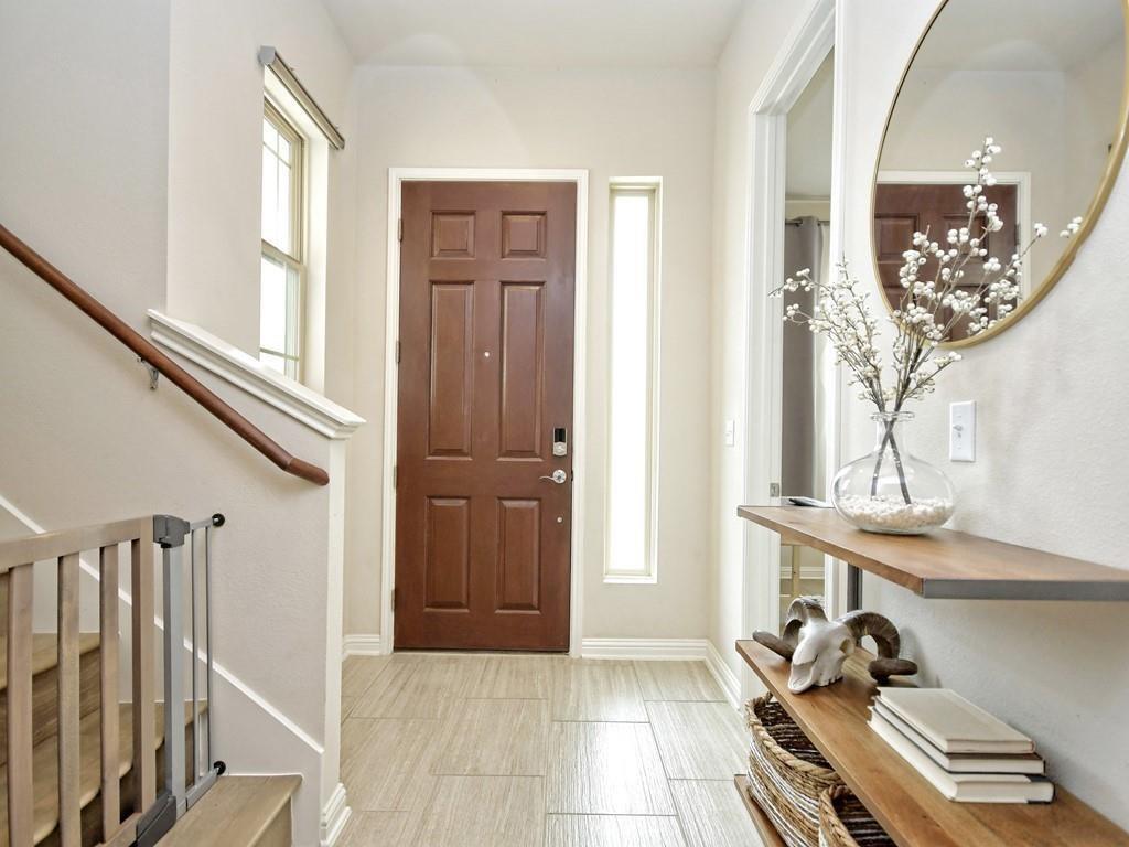 Bright entry foyer with a dark wood front door, narrow windows, and a staircase with a wood handrail.
