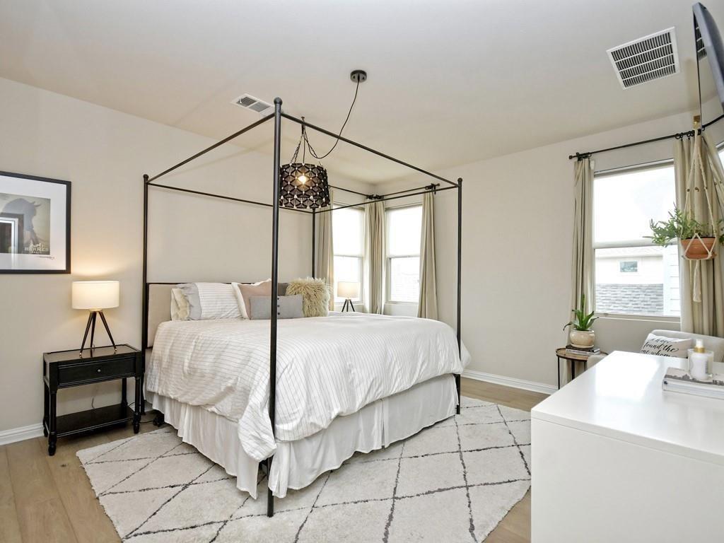 Bedroom with a black canopy bed, white bedding, geometric rug, and tall curtained windows.