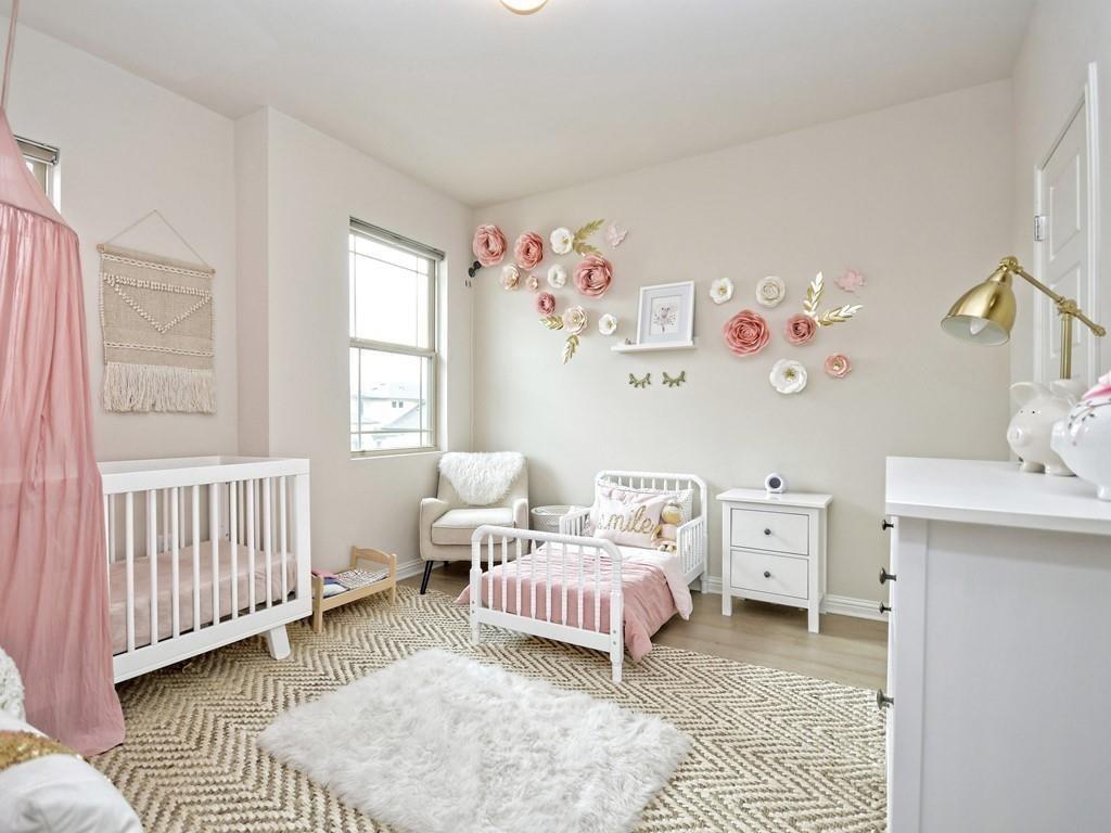 Nursery with two white cribs, pink bedding, floral wall decorations, and a cream rocking chair.