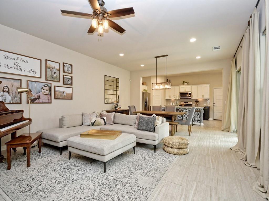 Living room with a gray sectional, patterned rug, piano, and open kitchen beyond.