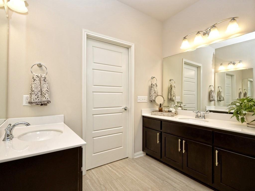 Bathroom with double dark-wood vanities, white counters, large mirrors, and a paneled door.