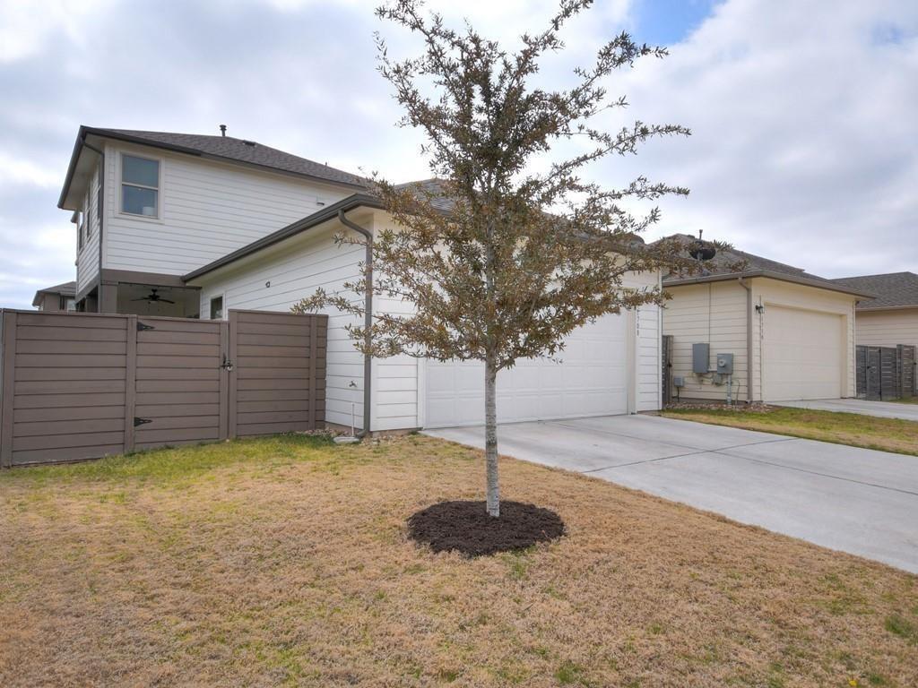 Two-story white house with an attached garage, fenced yard, and young tree in the lawn.