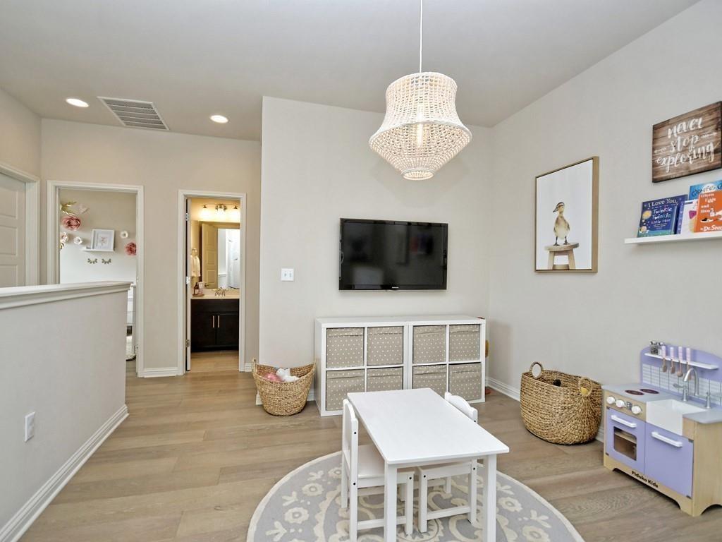 Children’s playroom with a small table, toy kitchen, woven baskets, and wall-mounted television.