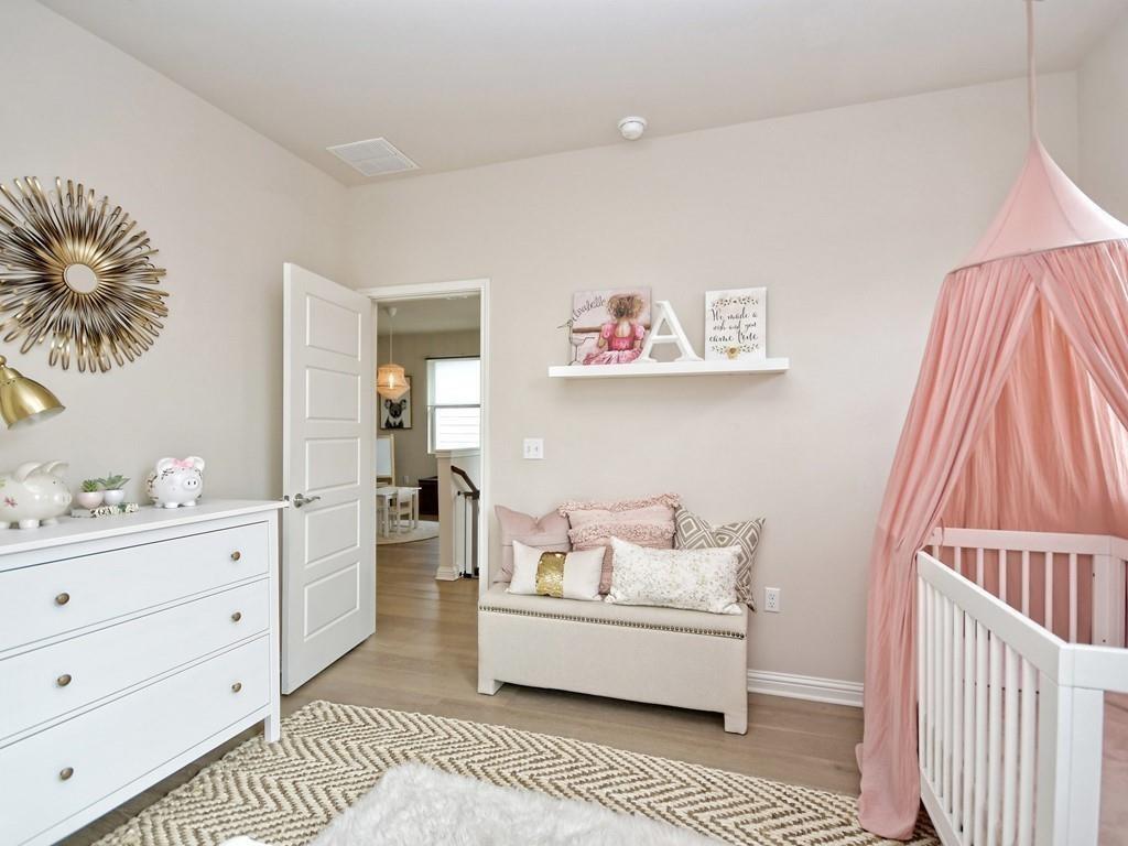 Nursery with a white crib under a pink canopy and a small upholstered settee.
