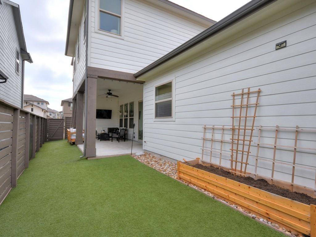 Fenced backyard with artificial turf, a covered seating patio, and a raised planter along the house.
