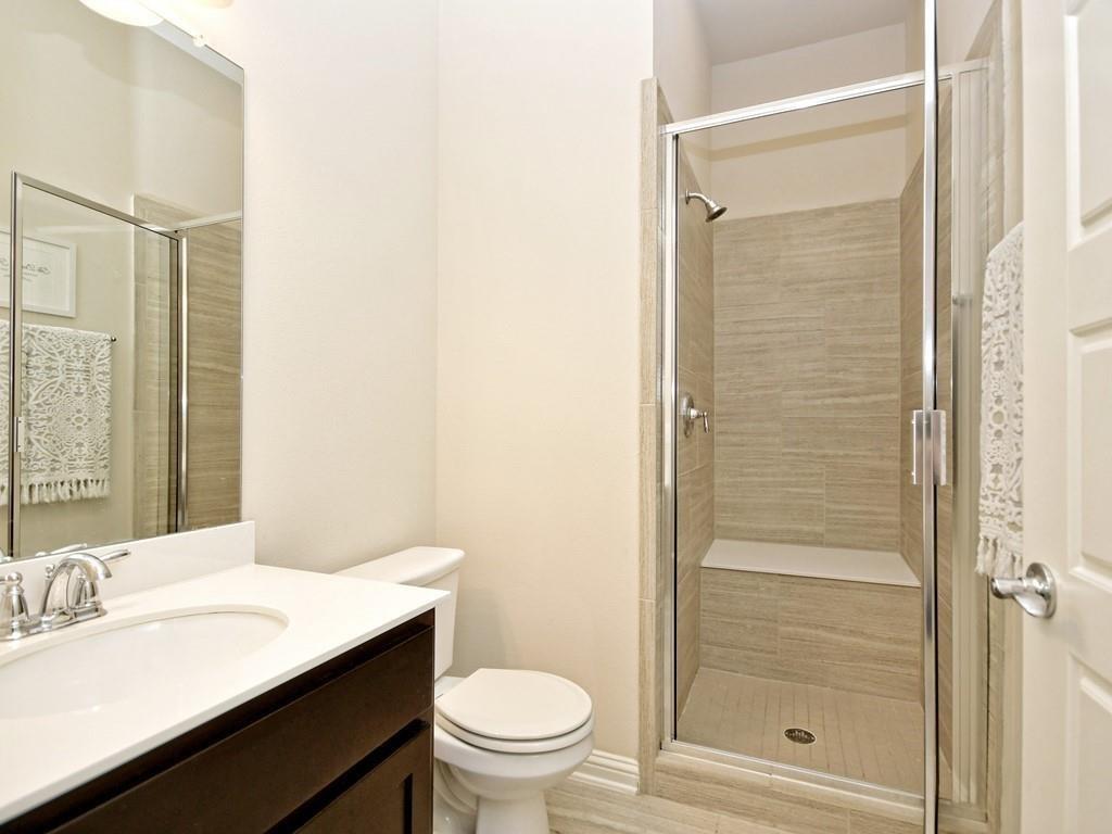 Bathroom with a glass-enclosed beige-tile shower beside a white vanity and toilet.