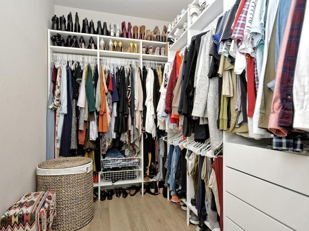 Walk-in closet with extensive clothing and shoe storage, a woven hamper, and white drawers.