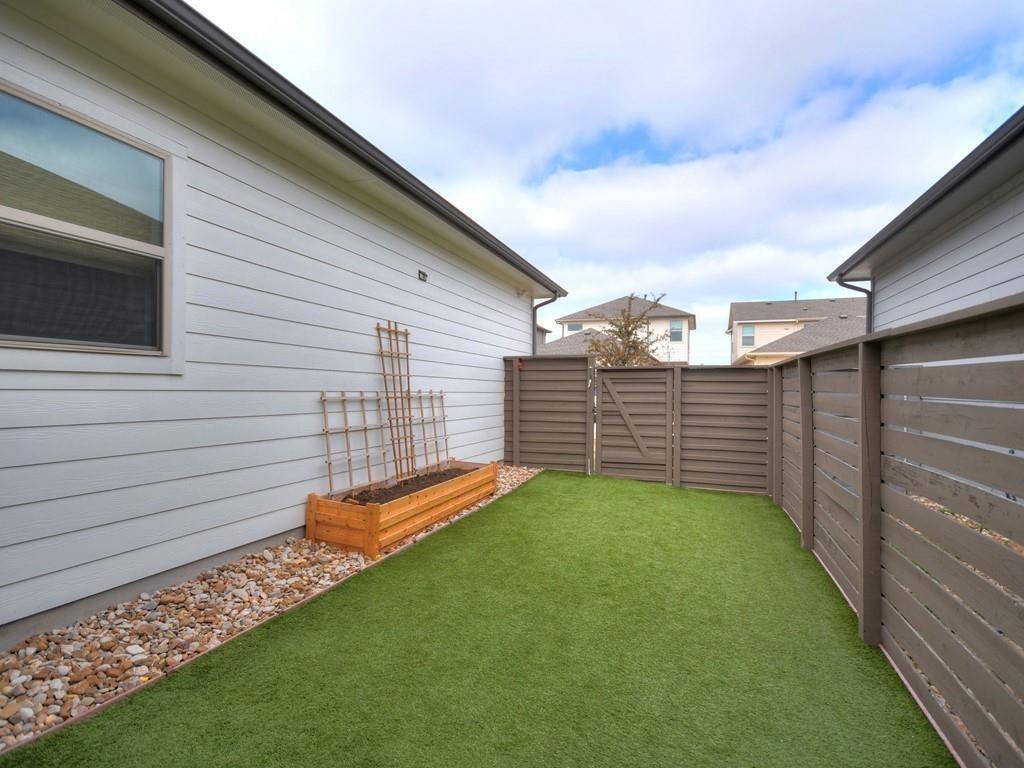 Enclosed backyard with artificial turf and a raised wooden planter bed.