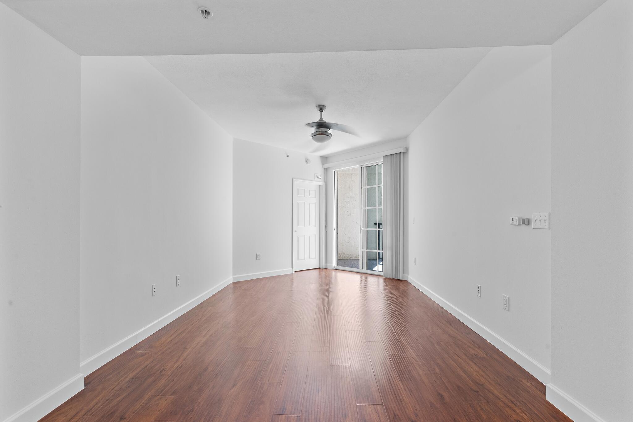 Empty room with wood-look flooring, a ceiling fan, and sliding glass doors to a patio.