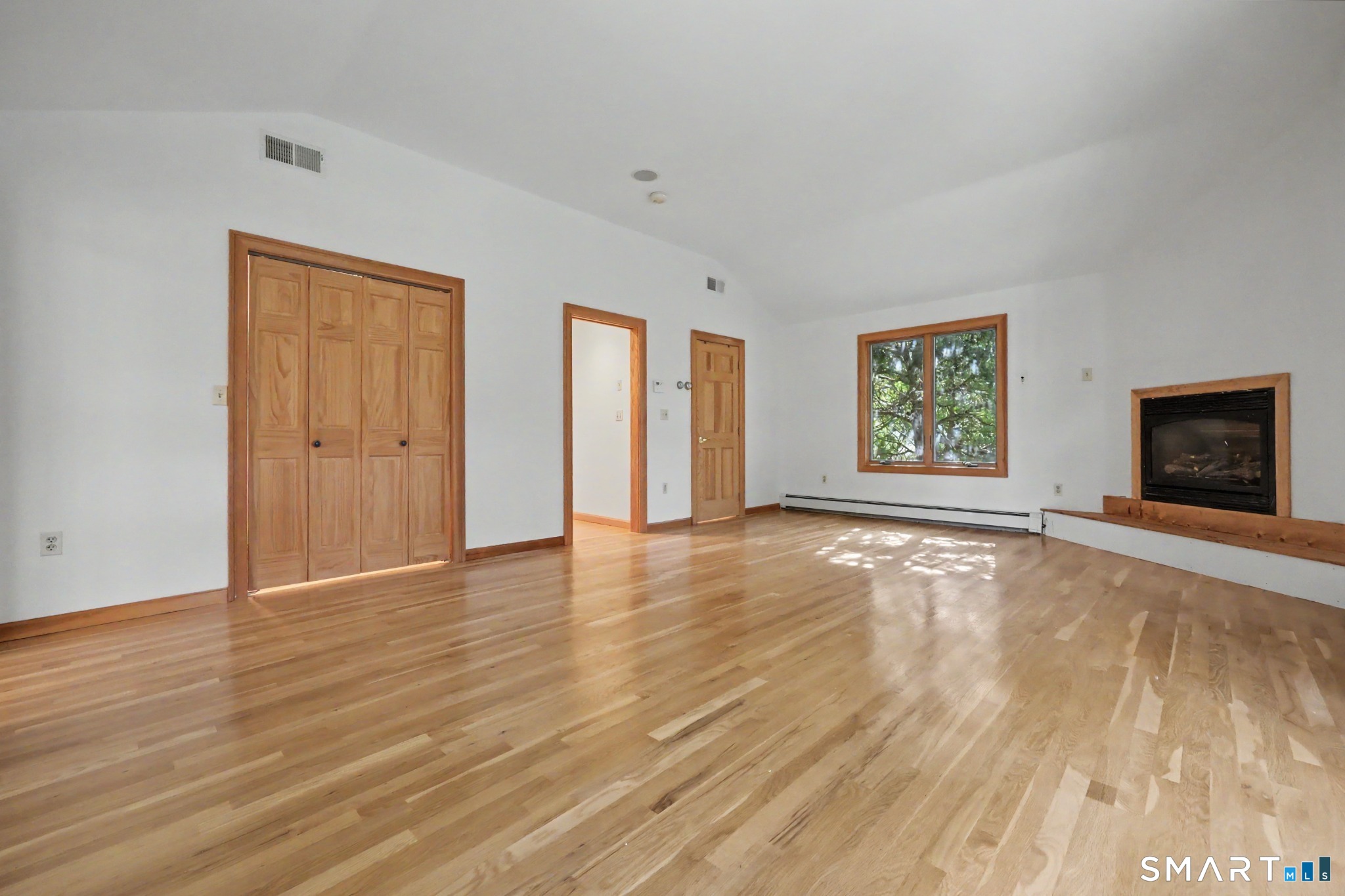 Empty living room with hardwood floors, wood-trimmed window, and built-in fireplace.