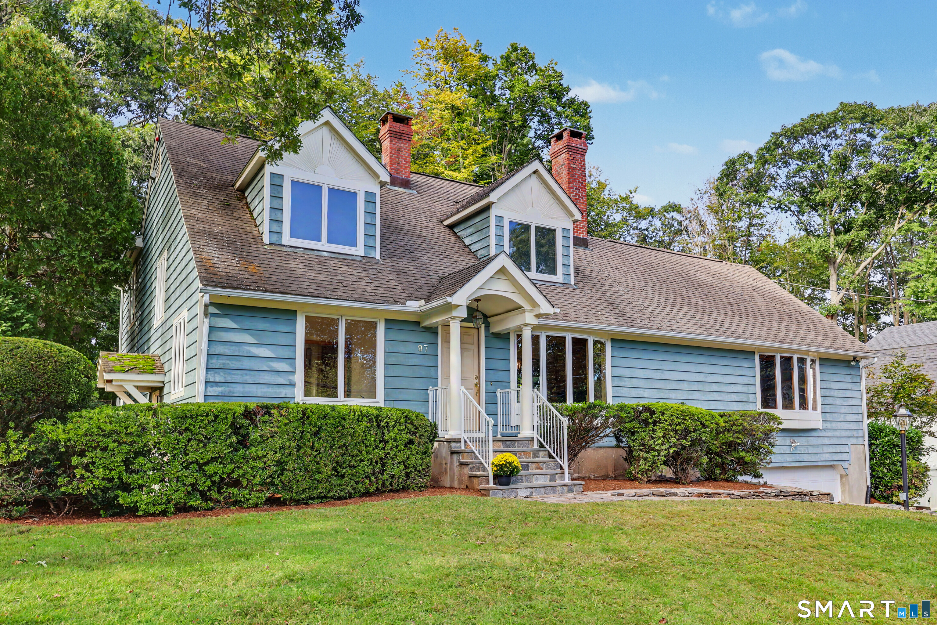 Blue-sided house with two dormers, brick chimneys, and a covered front entry.